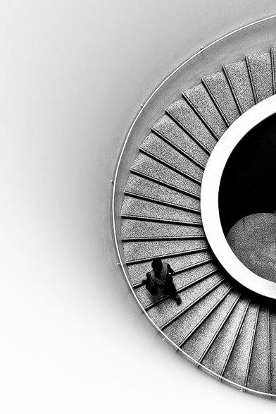 Spiral concrete staircase viewed from directly above, a single figure pausing at its base