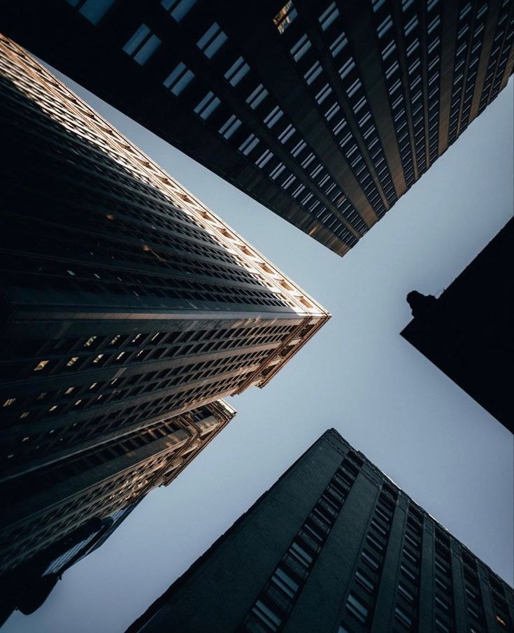 Looking straight up at converging glass towers against a pale sky